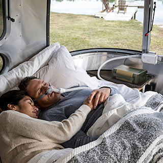 A man and a woman are sleeping while hugging each other with a CPAP machine in use.